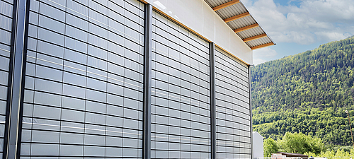 Tectura plegable delantera 3 grandes fachadas plegables en un almacén. Al fondo se ven montañas plantadas y un cielo azul.